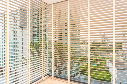 Beige built-in blinds through which greenery is seen.